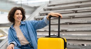 Beautiful Young Woman With Luggage Sitting On Stairs At Airport